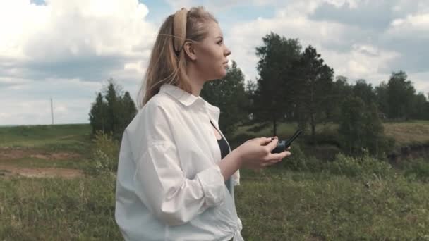 Meisje met een bedieningspaneel over een drone staat in een veld — Stockvideo