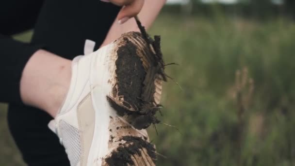 Meisje in een wit shirt en witte sneakers reinigt het vuil van de zool terwijl ze op een been staat, close-up — Stockvideo