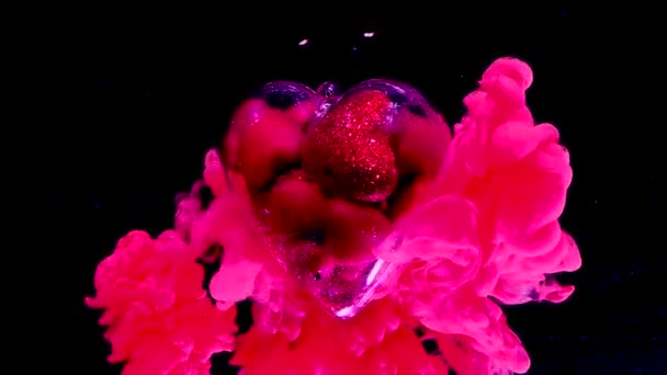schöne große Glasherz gefüllt mit kleinen roten Herzen dreht sich um seine Achse. Konzept für den Valentinstag am 14. Februar. rosa Tinte im Wasser auf schwarzem Hintergrund.