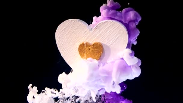 weißes Holzherz mit goldenem Herzen in der Mitte auf schönem Hintergrund. Konzept für den Valentinstag am 14. Februar. weiße und violette Tinte in Wasser auf schwarzem Hintergrund.