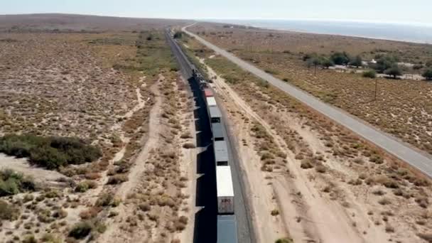 カリフォルニア砂漠の道路で貨物列車が移動する鉄道 バード トラッキング空中ビュー — ストック動画