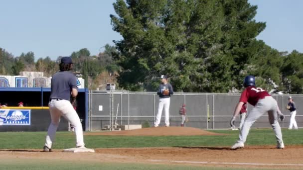 Střední škola baseball nadhazovač hází na první metu, jak hráč dělá běh na druhou metu — Stock video