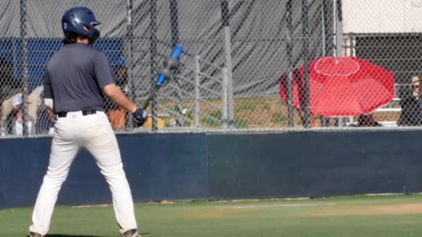 High school baseball batter athlete preparing to bat on sports field diamond. Rear shot. — Stock Video