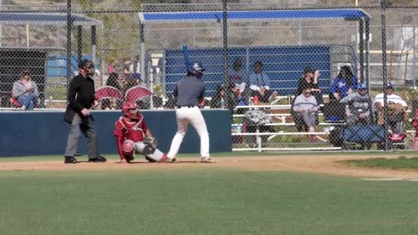 High school baseball player hits ball and runs to first base with catcher — Stock Video
