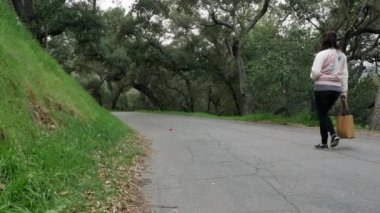 Bir kadın parkta tek başına yürüyor. Ağaçlar her yerde, ağır çekimde.