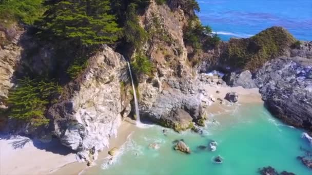 Aerial of Big Sur over a waterfall cascading from rocks down onto the beach — Stock Video