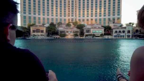 Вид отеля "Белладжио" на фонтаны воды и фасад отеля, проходящие мимо люди — стоковое видео