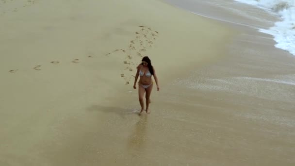 Gyönyörű napbarnított nő fürdőruhában séta a tengerparton hullámokban, légi kilátás — Stock videók