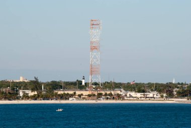 Key West 'in tarihi deniz feneri ve kumsaldaki telekomünikasyon kulesi manzarası (Florida).