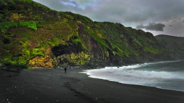 Sao Miguel Adası 'ndaki Mosteiros' ta (Azores, Portekiz) maceraperest bir sahil. Kara kalın bulutlar ve çalkalanan, fırtınalı ocenan dalgaları uğursuz ve tehlikeli bir şeyi işaret ediyor. Sadece canlı yeşil tepeler parlak gelecek için yeni bir umut verir.. 