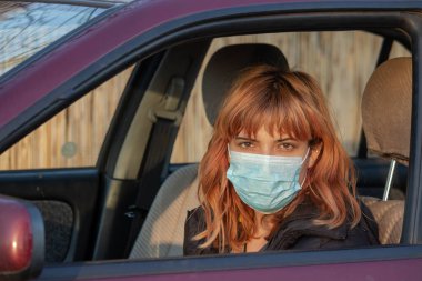 Arabada tıbbi maske takan bir kız. Corona virüsünden korunmak için maske takan, Covid-19 yazan bir kadın. Virüs salgını sırasında maskeli araç kullanmak. Günlük aktivitelerde maske takılmalıdır.