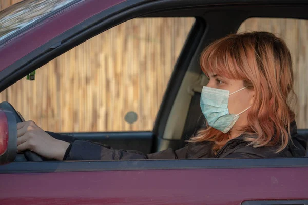 Girl wearing medical mask in the car. Woman wearing mask, written COVID-19, to protect from corona virus. Driving car with mask during virus pandemic. Mask must be put on in everyday activities.
