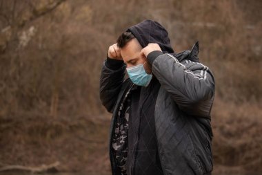 Onu Coronavirus 'tan korumak için maskeli bir adam. Corona virüsü salgını. Corona Sağlık Hizmetleri. Tıbbi maskeli genç bir adam doğada duruyor. Tıbbi maskeli bir kapüşonlu. Morina