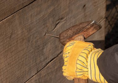 Çekiçli sarı eldiven çiviyi tahtaya çakıyor.