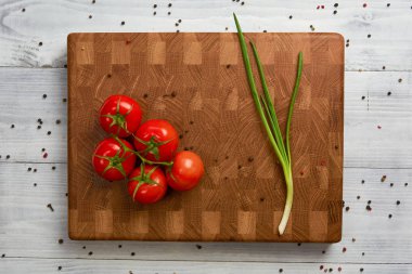 Tahta kesme tahtasında kırmızı taze domates ve yeşil soğan.