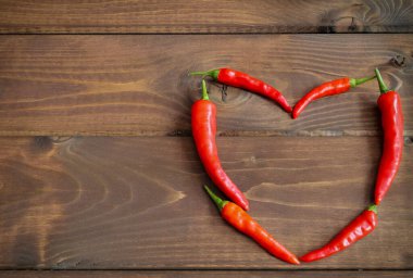 Kahverengi ahşap arka planda kırmızı biberden yapılmış kalp şekli. Metnin için boş alanı olan en üstteki görünüm