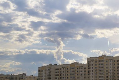 Güzel bulutlu gökyüzü, çok katlı evlerin üzerinden geçen bir uçağın beyaz izi. Şehir manzarası