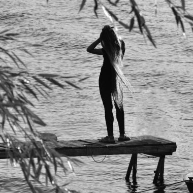 Sahil nehrinde uzun saçlı bir kız. Arkadan uzun, güneşli bir manzara.