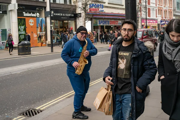 Londra - 7 Mart 2020: Şehirde alışveriş yapan insanlar ve saksafonlu müzik karıncaları