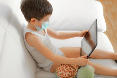 Yüzü maskeli küçük çocuk tablet gibi görünüyor.