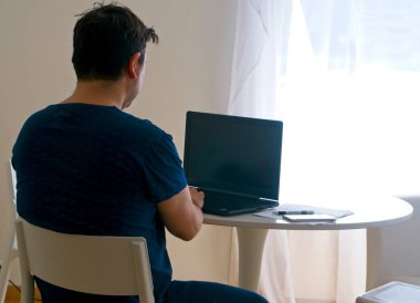 Genç adam evde oturup dizüstü bilgisayarla çalışıyor. Çalışan baba konsepti. Telesekreter kavramı