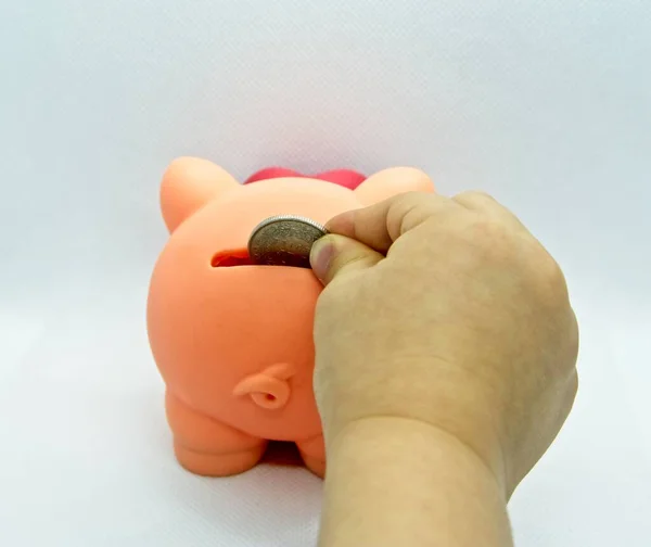 Hand of a person introducing a coin into a plastic piggy bank in a white background