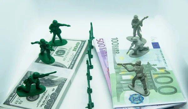Miniature plastic figure of soldiers on top of two bundles, one made of dollar bills and the other of euros with a plastic ditch in the middle