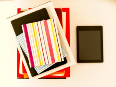 Beyaz arkaplanlı bir e-kitabın yanında kitap ve ders kitapları yığını