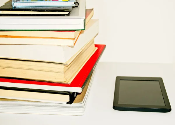 Pile of text books and books next to an e-book on a white background