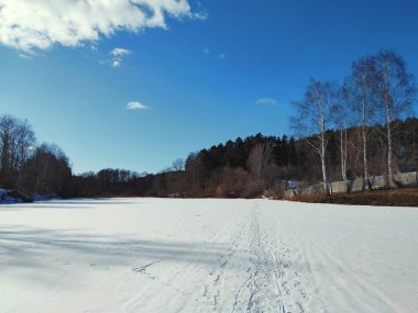 Kışın kış uykusundan sonra henüz çözülmemiş bir göleti olan güneşli bir pınar. Güzel ağaçların ve mavi gökyüzünün arka planında üzerinde güzel bir patika var.