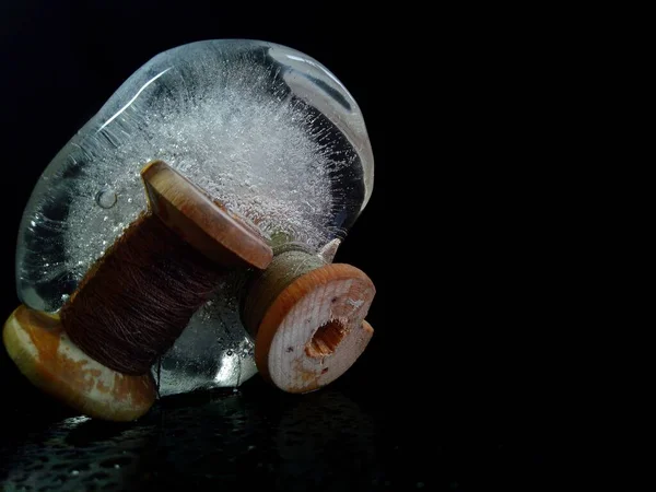 two old wooden bobbins with threads frozen in a piece of ice on a black background in a creative macro photo