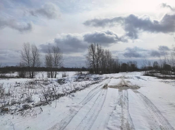 a gloomy spring landscape with a road leading along the river, not yet woken up from a winter dream against a blue sky with beautiful clouds