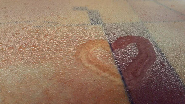 a heart drawn on wet glass with water drops and an abstract background