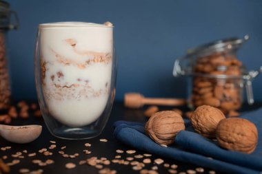 Sağlıklı kahvaltı yoğurdu, yulaf ezmesi, ceviz, badem ve fındık. Açık bir bardakta bal, koyu mavi arka planda çift duvarlı.