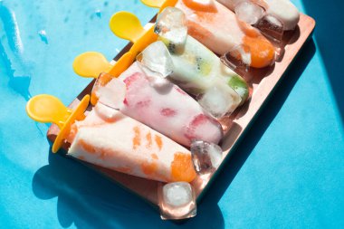 Ev yapımı dondurmayı bir çubuğa koyup, buzda meyveler, ahşap tepside mavi bir arka planda, buz parçalarına ayırın.