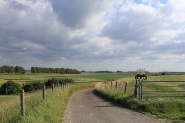 Zeeland, Hollanda 'daki batısal denizi aşan bir hendekten görünen büyük yeşil tarlalar ve ilkbaharda arkasında bir sürü bulut olan güzel bir fırtınalı gökyüzü.