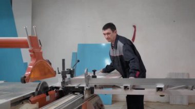 Yetişkin bir erkek işçi, marangozluk atölyesinde çalışıyor. Tahtayı elektrikli testereyle kesiyor..
