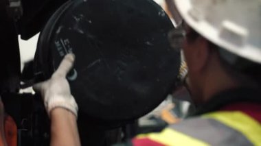 Tamirci kamyondaki filtreyi değiştiriyor. Kask, yansıtıcı yelek, gözlük ve eldiven takıyor. Güvenlik için..