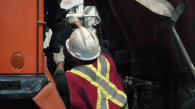 Tamirci kamyondaki filtreyi değiştiriyor. Kask, yansıtıcı yelek, gözlük ve eldiven takıyor. Güvenlik için..