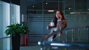 Koyu saçlı, akıllı telefonuyla konuşan ve kahve içen güzel bir kız. Ofiste..