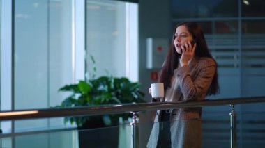 Koyu saçlı, akıllı telefonuyla konuşan ve kahve içen güzel bir kız. Ofiste..
