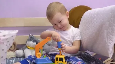 Çekici bebek yatakta oturur ve cıvataları çevirir oyuncak bir arabada.