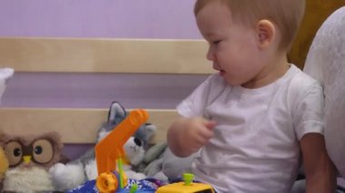 Çekici bebek yatakta oturur ve cıvataları çevirir oyuncak bir arabada.