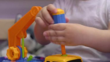 Çekici bebek yatakta oturur ve cıvataları çevirir oyuncak bir arabada.