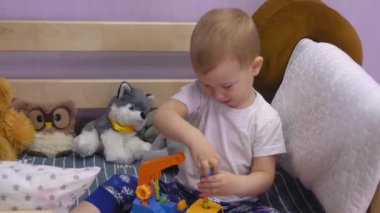 Çekici bebek yatakta oturur ve cıvataları çevirir oyuncak bir arabada.