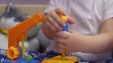 Çekici bebek yatakta oturur ve cıvataları çevirir oyuncak bir arabada.