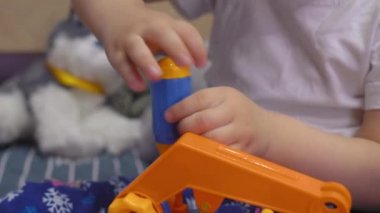 Çekici bebek yatakta oturur ve cıvataları çevirir oyuncak bir arabada.