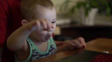 Küçük çocuk dizüstü bilgisayarında yazarken eğleniyor. Annesi yanına oturur ve güler. Zaman zaman çocuk çok şaşırır ve parmağıyla ekranı gösterir..
