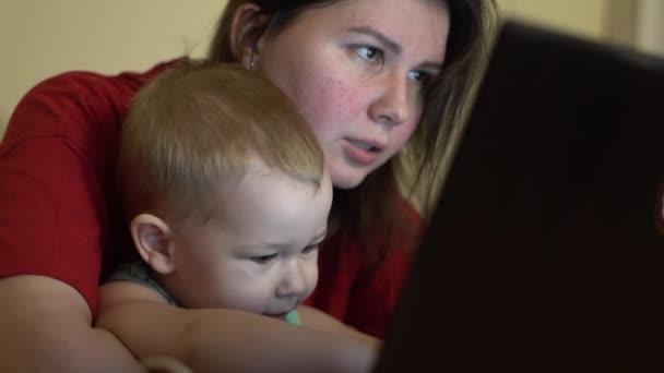 その少年はノートパソコンに入力するのが楽しい 母親は隣に座って笑っている 時々少年は非常に驚いていると彼の指で画面でポイントします — ストック動画