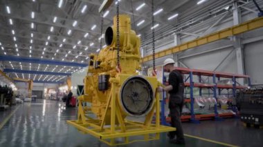 Magadan, Rusya - 15 Ağustos 2019. Ağır ekipmanlar için motor ve şanzıman yenileme fabrikası. Miğferli işçiler motoru vinçle taşıyorlar..